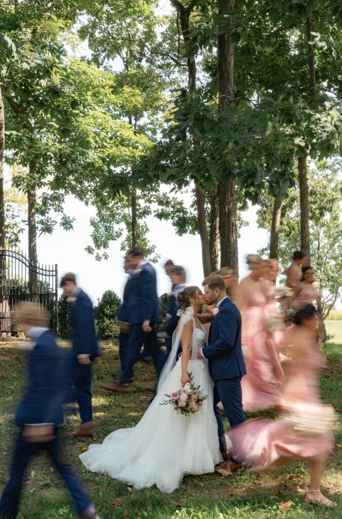 Documentary style wedding portrait of a bride and groom with motion blur around them as bridesmaids and groomsmen surround them at Lizton Lodge venue in Central Indiana.